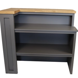 May include: A grey corner bar unit with a wood top and two shelves. The unit has a small backsplash and is made of wood.