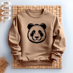 May include: A tan sweatshirt with a black panda face design. The panda's face is centrally placed, with detailed fur and facial features. The sweatshirt has a crew neck and ribbed cuffs and hem.