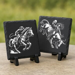 May include: Two black slate coasters with white illustrations of a cowboy riding a horse and a rodeo rider on a bull. The coasters are square and sit on small black stands.