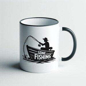 K&ouml;nnte beinhalten: Wei&szlig;e Keramiktasse mit schwarzem Rand und Henkel. Die Tasse zeigt eine schwarze Silhouette einer Person, die von einem Boot aus angelt, mit dem Text "Gone Fishing".