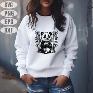 May include: White sweatshirt with a black and white panda bear illustration holding bamboo. The panda is surrounded by bamboo stalks. The sweatshirt has a black trim around the neckline. The image also includes the text "SVG", "PNG", "EPS", and "DXF".