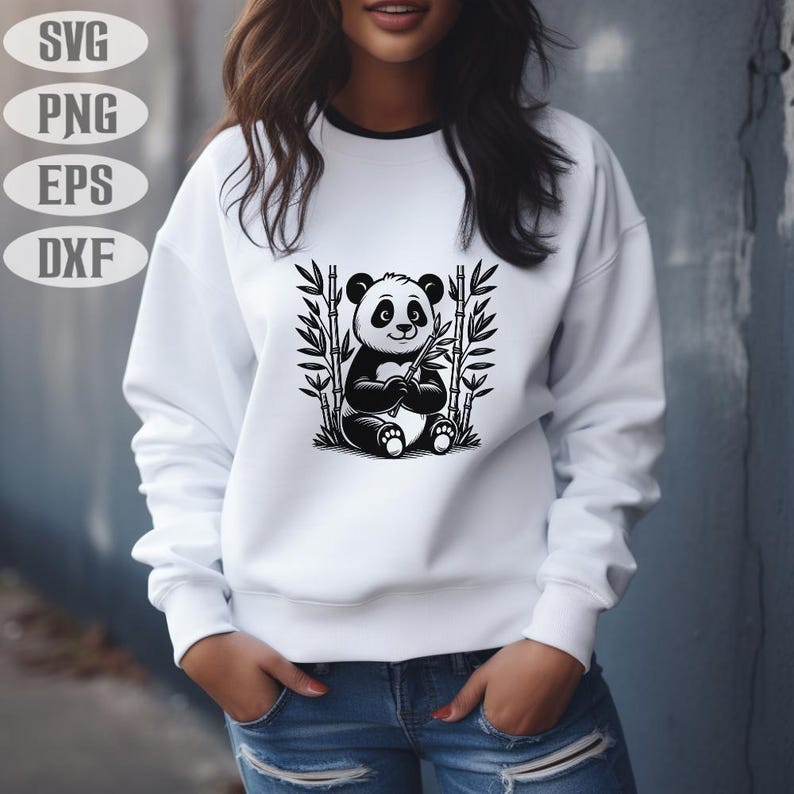 May include: White sweatshirt with a black and white panda bear illustration holding bamboo. The panda is surrounded by bamboo stalks. The sweatshirt has a black trim around the neckline. The image also includes the text "SVG", "PNG", "EPS", and "DXF".