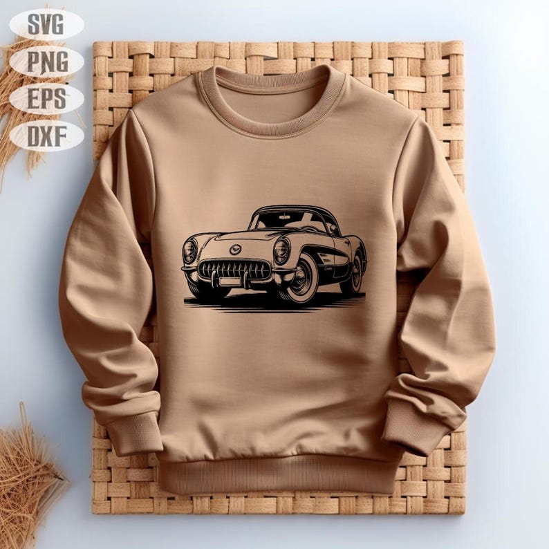 May include: A tan sweatshirt featuring a black and white illustration of a classic car. The car is a vintage model with detailed headlights, grille, and wheels. The sweatshirt has a crew neck and long sleeves, and is displayed on a woven background.