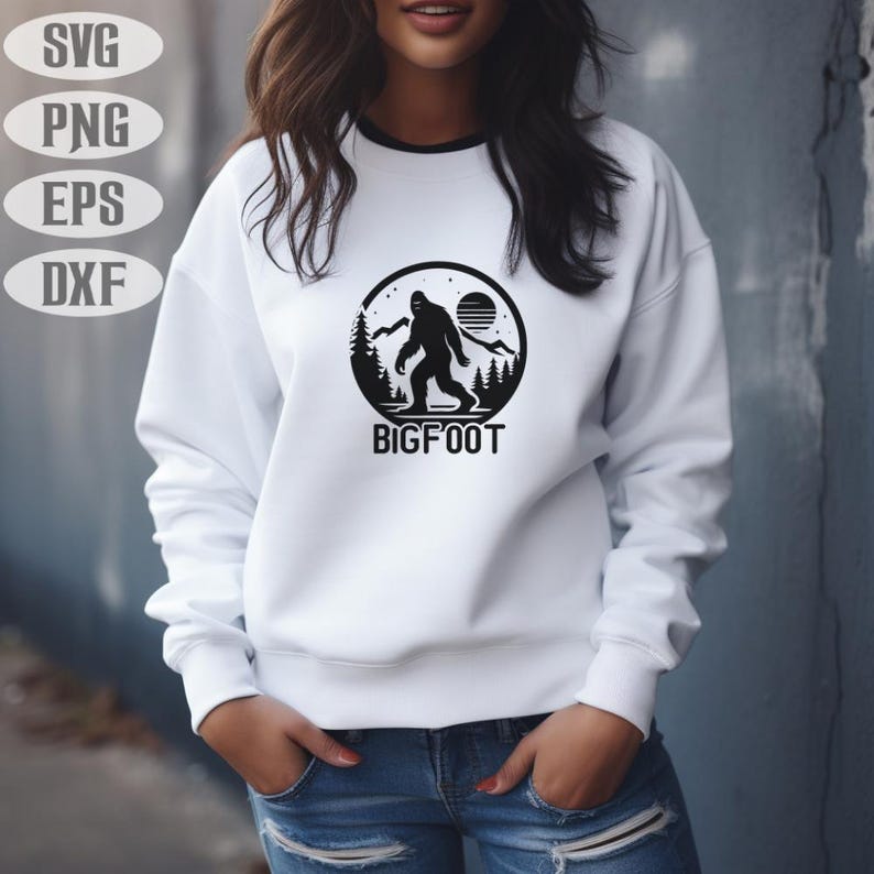 May include: White sweatshirt with a black Bigfoot graphic. The graphic features a silhouette of Bigfoot in a forest scene with a sun and the word "BIGFOOT". The sweatshirt has a black trim around the neckline.