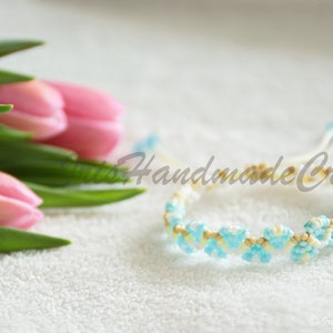 K&ouml;nnte beinhalten: Ein wei&szlig;es und blaues Freundschaftsarmband mit einem gewebten Muster. Das Armband ist aus kleinen Perlen gefertigt und hat ein hellblaues und wei&szlig;es Farbschema.