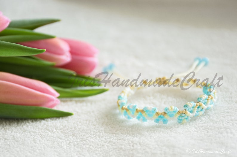 K&ouml;nnte beinhalten: Ein wei&szlig;es und blaues Freundschaftsarmband mit einem gewebten Muster. Das Armband ist aus kleinen Perlen gefertigt und hat ein hellblaues und wei&szlig;es Farbschema.