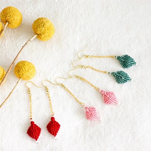 May include: Three pairs of dangle earrings with beaded tassels. The earrings are red, pink, and green. The earrings are hanging from gold chains.