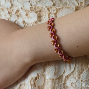 K&ouml;nnte beinhalten: Ein geflochtenes Freundschaftsarmband in Pink und Braun. Das Armband wird am Handgelenk getragen.