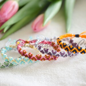 K&ouml;nnte beinhalten: F&uuml;nf bunte Freundschaftsb&auml;nder mit geometrischen Mustern in Gr&uuml;n-, Blau-, Gelb-, Rosa-, Lila-, Orange- und Schwarzt&ouml;nen. Die Armb&auml;nder sind mit einer Knotentechnik hergestellt und haben einen einfachen Verschluss zum Binden.