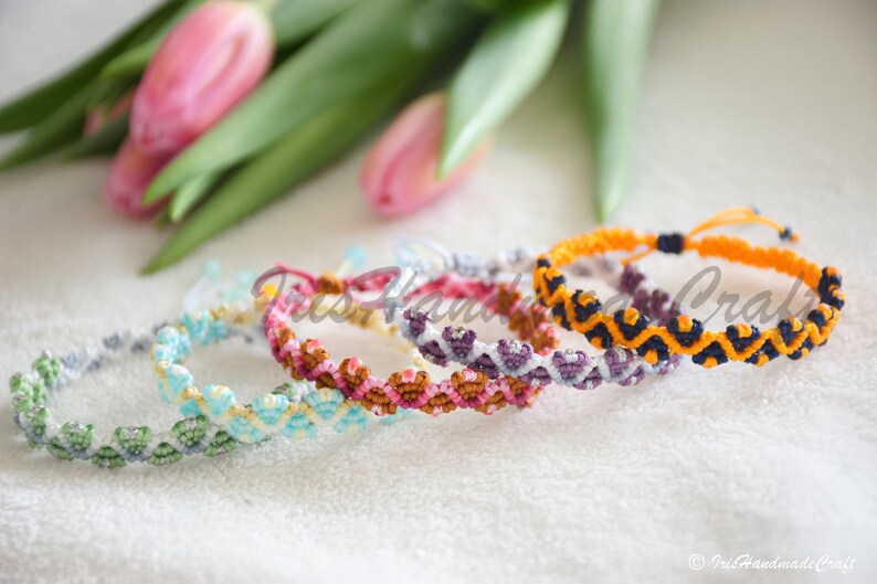 K&ouml;nnte beinhalten: F&uuml;nf bunte Freundschaftsb&auml;nder mit geometrischen Mustern in Gr&uuml;n-, Blau-, Gelb-, Rosa-, Lila-, Orange- und Schwarzt&ouml;nen. Die Armb&auml;nder sind mit einer Knotentechnik hergestellt und haben einen einfachen Verschluss zum Binden.