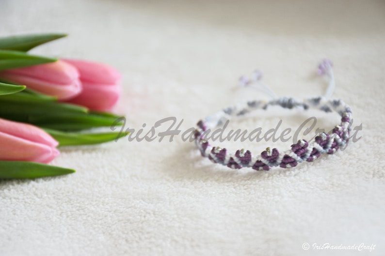 K&ouml;nnte beinhalten: Ein wei&szlig;es und violettes Freundschaftsarmband mit einem Chevron-Muster. Das Armband ist mit einer Knotentechnik hergestellt und hat einen zarten, femininen Look.