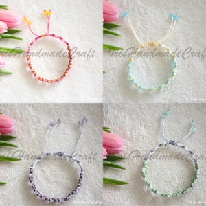 K&ouml;nnte beinhalten: Vier handgefertigte Freundschaftsarmb&auml;nder mit verschiedenen farbigen Perlen und Schn&uuml;ren. Die Armb&auml;nder sind mit einem Knoten gebunden und haben an jedem Ende einen Quasten. Die Armb&auml;nder werden auf einem wei&szlig;en Hintergrund mit rosa Tulpen pr&auml;sentiert.