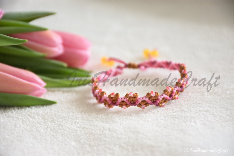 K&ouml;nnte beinhalten: Ein pinkfarbenes und braunes Freundschaftsarmband mit einem gewebten Muster. Das Armband ist mit einer Knotentechnik hergestellt.
