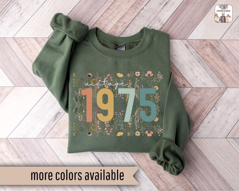 Puede incluir: Una sudadera verde con un dise&ntilde;o floral y el texto "vintage 1975" en letras de colores.