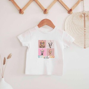 Op de afbeelding: Wit T-shirt met een kleurrijke afbeelding van dieren die feestmutsen dragen. De tekst "Party at the Zoo" is onder de afbeelding gedrukt.