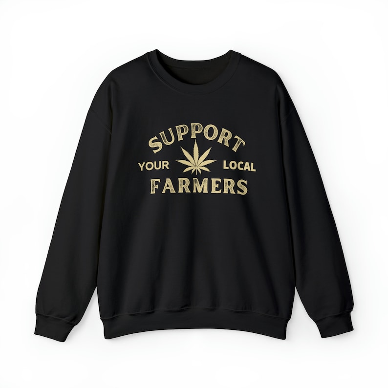 Puede incluir: Sudadera negra con un gr&aacute;fico dorado que dice "Apoya a tus agricultores locales" con una hoja de marihuana en el centro.