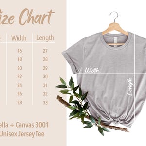 Puede incluir: Tabla de tallas para una camiseta de jersey unisex, que muestra las medidas de ancho y largo en pulgadas para las tallas XS a 3XL. La tabla est&aacute; impresa sobre un fondo marr&oacute;n claro con una camiseta gris colgada de una percha de madera.