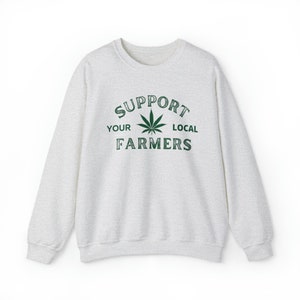 Puede incluir: Una sudadera gris jaspeada con un gr&aacute;fico de hoja de marihuana verde y el texto "Support Your Local Farmers".