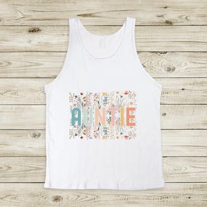 May include: White tank top with a floral design and the word "AUNTIE" in colorful letters.