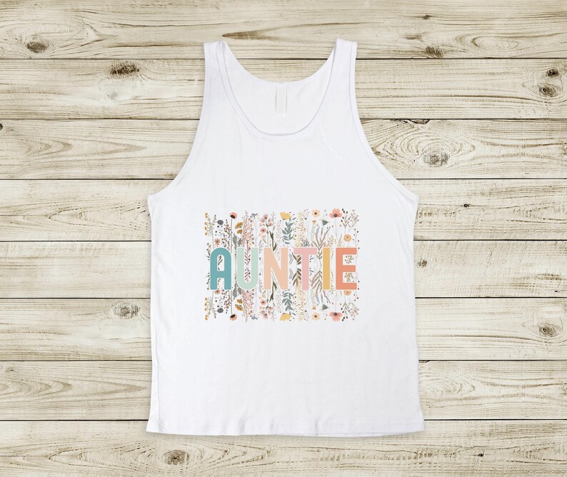 May include: White tank top with a floral design and the word "AUNTIE" in colorful letters.