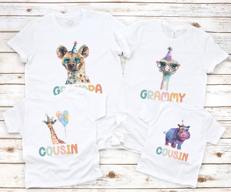 May include: Four white t-shirts with colorful animal graphics and text. The shirts feature a hyena, an ostrich, a giraffe, and a hippopotamus. The text on the shirts reads "Grandpa", "Grammy", "Cousin", and "Cousin".