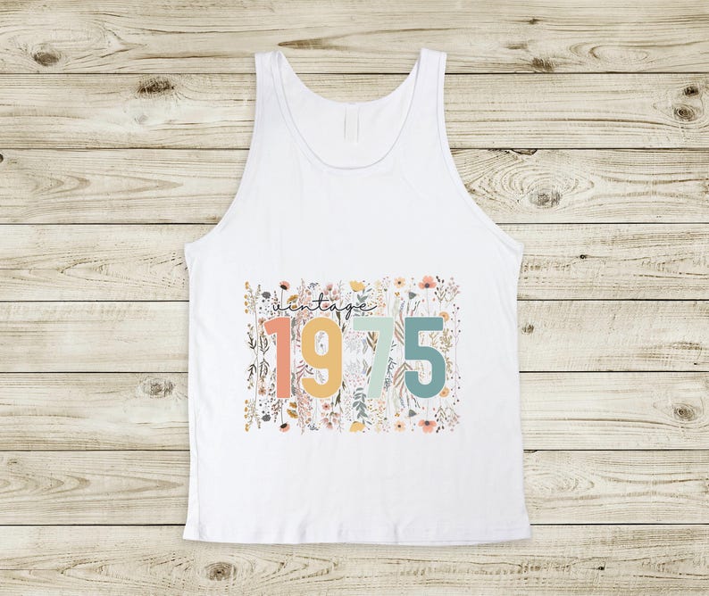 Puede incluir: Camiseta sin mangas blanca con un dise&ntilde;o floral y el texto "vintage 1975" en letras de colores.