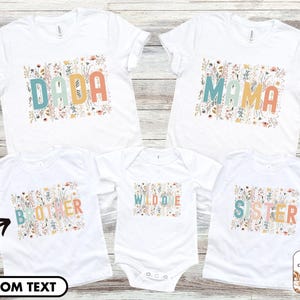 May include: Five white t-shirts with floral designs and text. The shirts say "Dada", "Mama", "Wild One", "Brother", and "Sister".