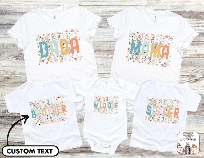 May include: Five white t-shirts with floral designs and text. The shirts say "Dada", "Mama", "Wild One", "Brother", and "Sister".