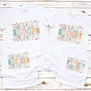 May include: Four white t-shirts with floral designs and text. The shirts say "Grandpa", "Grammy", "Brother", and "Birthday Girl".