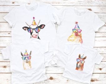 May include: Four white t-shirts with different animal illustrations wearing party hats and sunglasses. The animals are a cow, a chicken, a llama, and a horse.