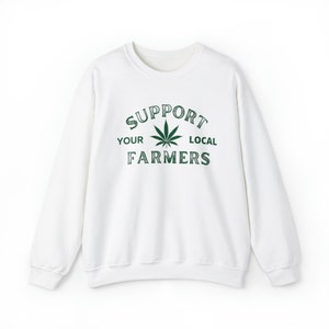 Puede incluir: Sudadera blanca con un gr&aacute;fico de hoja de marihuana verde y el texto "Support Your Local Farmers".