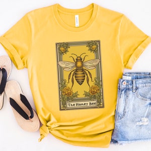 May include: A yellow t-shirt with a vintage illustration of a honey bee in a frame. The text "The Honey Bee" is printed below the image.