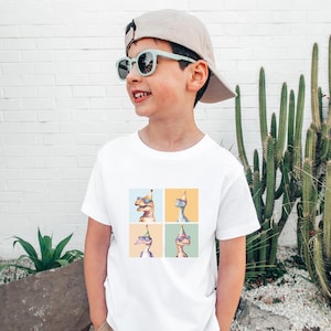 Puede incluir: Una camiseta blanca con un gr&aacute;fico de cuatro dinosaurios que llevan sombreros de fiesta y gafas de sol. Los dinosaurios est&aacute;n en un patr&oacute;n de cuadr&iacute;cula en la camiseta. La camiseta la lleva un ni&ntilde;o que lleva una gorra de b&eacute;isbol beige y gafas de sol azules.