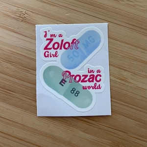 May include: White sticker sheet with two pill-shaped designs and text. One design reads "I'm a Zoloft Girl" with a blue pill that says "50 MG". The other says "in a Prozac world" with a green pill that says "88".