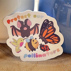 May include: A vibrant sticker with illustrations of a bat, butterfly, hummingbird, bee, and ladybug. The text "protect our pollinators" is in a rainbow font. The bat is dark grey with pink wings, and the butterfly is orange and black.