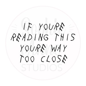 May include: Black and white text on a white background in a circle. The text reads "If you're reading this you're way too close" with the words "Sophie Jane Studios" below.