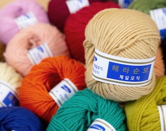 Könnte beinhalten: Nahaufnahme einer Vielzahl von Garnknäueln in verschiedenen Farben, darunter Rosa, Rot, Orange, Gelb, Grün, Blau und Beige. Die Garnknäuel sind zu einem Stapel angeordnet, und das Etikett auf dem beigen Garnknäuel lautet "헤라 순모 제일모직".
