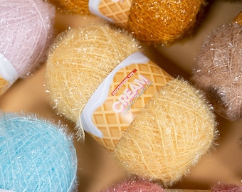 May include: Assortment of colorful yarn skeins with a fuzzy texture. The yarn is labeled "CREAM" with a waffle cone design.