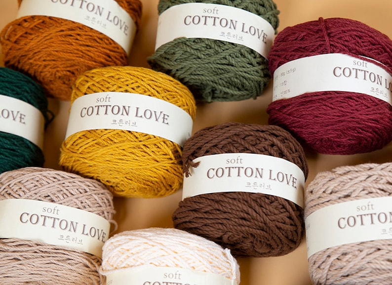 Puede incluir: Una colecci&oacute;n de ovillos de lana en varios colores, incluyendo amarillo mostaza, rojo oscuro y verde oliva. Cada ovillo est&aacute; etiquetado con "soft COTTON LOVE" en ingl&eacute;s y coreano. La lana est&aacute; bien enrollada, lo que sugiere que es adecuada para proyectos de tejido o ganchillo.