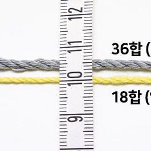Puede incluir: Dos hebras de hilo, una gris y otra amarilla, se muestran junto a una regla. El hilo gris es m&aacute;s grueso, etiquetado como 36합 (aproximadamente 2,5 mm), mientras que el hilo amarillo es m&aacute;s delgado, etiquetado como 18합 (aproximadamente 1,5 mm).