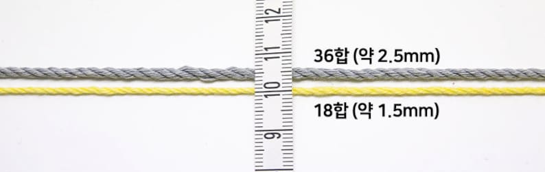 Puede incluir: Dos hebras de hilo, una gris y otra amarilla, se muestran junto a una regla. El hilo gris es m&aacute;s grueso, etiquetado como 36합 (aproximadamente 2,5 mm), mientras que el hilo amarillo es m&aacute;s delgado, etiquetado como 18합 (aproximadamente 1,5 mm).
