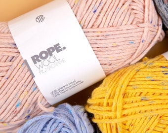 Può includere: Tre gomitoli di lana rosa, giallo e blu con macchie di colore. Il gomitolo rosa ha un'etichetta che recita "ROPE. WOOL ft. MACRAME 60% Lana merino 22% Acrilico premium 18% Super poliammide".