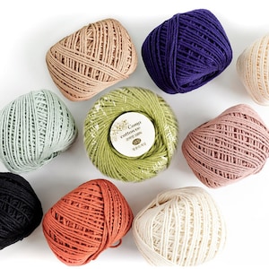 Może przedstawiać: Zestaw 10 kłębków bawełnianej przędzy w różnych kolorach, w tym zielonym, fioletowym, beżowym, białym, pomarańczowym i różowym. Przędza jest oznaczona jako "Coma cotton 100" i "150g".