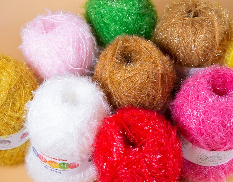 May include: A collection of colorful yarn balls with a sparkly, fuzzy texture. The yarn is arranged in a circle with the labels facing outward. The labels are in Korean and English.