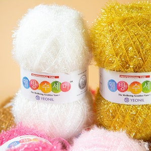 May include: A close-up of two spools of colorful scrubbing yarn. The spools are labeled "The Wellbeing Scrubber Yarn" and "Yeonil".