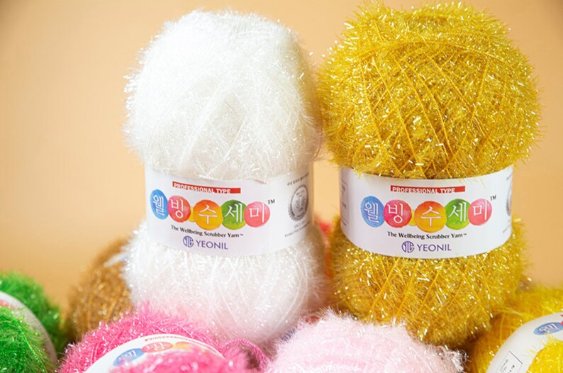 May include: A close-up of two spools of colorful scrubbing yarn. The spools are labeled "The Wellbeing Scrubber Yarn" and "Yeonil".