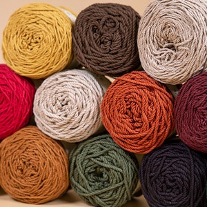 Puede incluir: Una colecci&oacute;n de ovillos de lana coloridos en varios tonos, incluyendo amarillo, rojo, marr&oacute;n y verde. La lana est&aacute; bien enrollada, algunos ovillos tienen etiquetas. La imagen muestra una variedad de colores adecuados para proyectos de tejido o ganchillo.