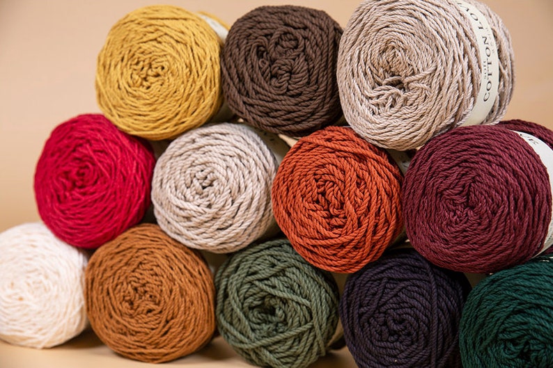 Puede incluir: Una colecci&oacute;n de ovillos de lana coloridos en varios tonos, incluyendo amarillo, rojo, marr&oacute;n y verde. La lana est&aacute; bien enrollada, algunos ovillos tienen etiquetas. La imagen muestra una variedad de colores adecuados para proyectos de tejido o ganchillo.