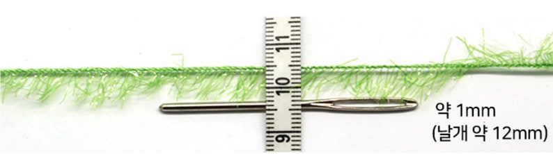 May include: A green fuzzy trim with a needle measuring approximately 1 inch (2.5 cm) in length. The trim is about 12 mm wide.