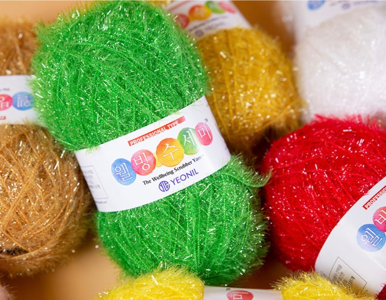 May include: Assortment of colorful scrubbing yarn balls. The yarn is made of a textured material and is designed for cleaning. The label reads "The Wellbeing Scrubber Yarn YEONIL".